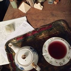 a tea cup and saucer sitting on top of a wooden table next to an open book