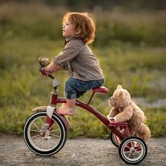 a little boy riding a bike with a teddy bear on the handlebars in front of him