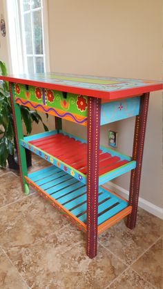 a colorful painted table in the corner of a room with a potted plant behind it