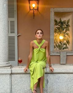 a woman in a green dress sitting on a ledge next to a lamp and window