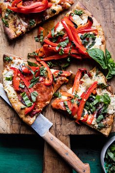 slices of pizza with red peppers, cheese and greens on a cutting board next to a knife