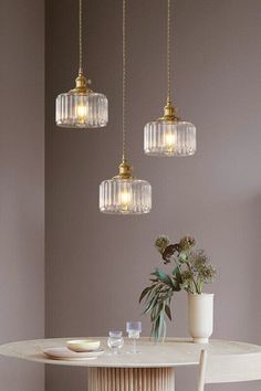 three glass pendant lights hanging over a white table with two vases on the side