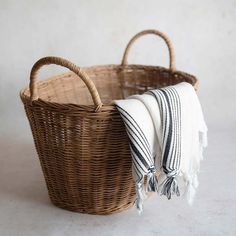 a wicker basket with two white and black striped towels in the bottom one is holding a folded towel