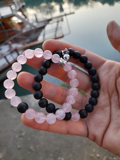 a person holding two bracelets with black beads and pink glass beads on each strand