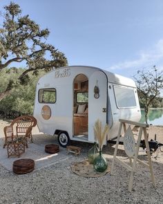 an old camper is parked on the side of the road with chairs around it