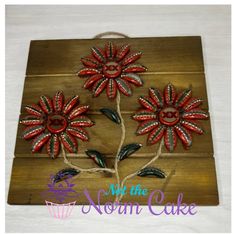 a wooden plaque with three red flowers on it's side and the words not the norm cake written below