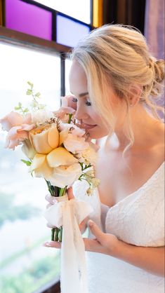 a woman in a white dress holding a bouquet of flowers and looking at the window