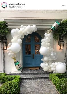 a blue front door with white balloons on it and a champagne bottle in the doorway