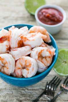 a blue bowl filled with shrimp and garnished with lime wedges next to a fork