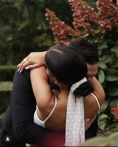 two people hugging each other in front of flowers