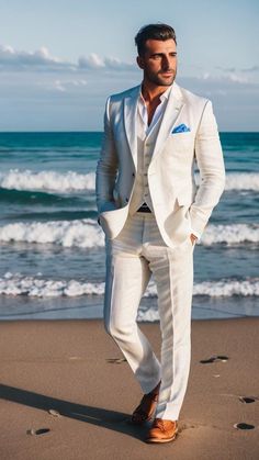 a man in a white suit standing on the beach with his hands in his pockets