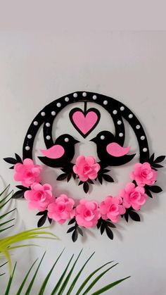 a metal wall hanging with pink flowers and two black birds on it's face