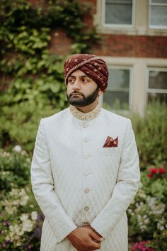 a man wearing a turban and standing in front of some flowers with his hands on his hips