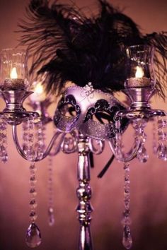 a fancy chandelier with candles and feathers on the top, in front of a wall