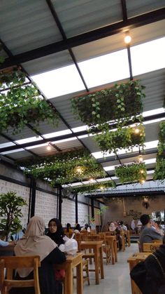 people are sitting at tables with plants growing on the ceiling and covering them from the sun