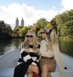 two women sitting on the back of a boat in front of a lake with trees