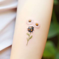 a ladybug tattoo on the back of a woman's arm with daisies