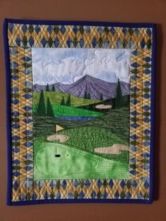 a quilted wall hanging with a golf course and mountains in the background on a brown wall