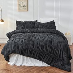 a bed with black comforter and pillows in a white room next to a wooden floor