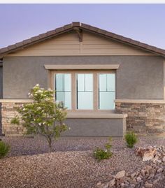 a house that is in the middle of some rocks and gravel with a small tree