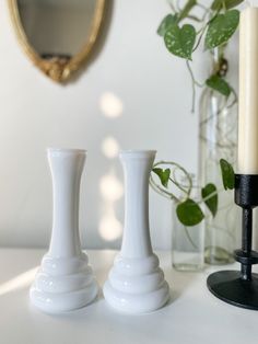 two white vases sitting on top of a table next to a mirror and candle