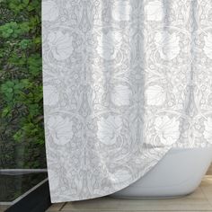 a bath tub sitting next to a window covered in white shower curtaines and green plants