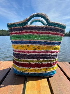 a multicolored bag sitting on top of a wooden table next to water and trees