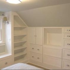 an empty bedroom with white cabinets and drawers in the corner, next to a window