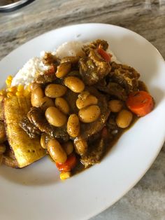 a white plate topped with meat, beans and rice