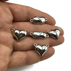 five silver heart charms in the palm of someone's hand