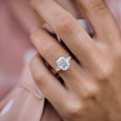 a woman's hand with a diamond ring on her finger and a pink shirt