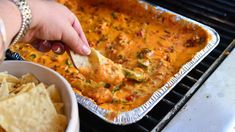 a person dipping tortilla chips into a casserole