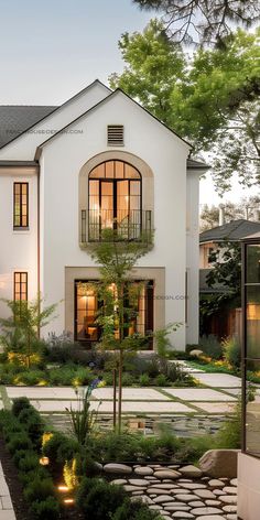 a large white house with lots of windows and plants in the front garden area at dusk