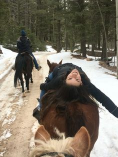 two people are riding horses in the snow and one person is laying down on the ground