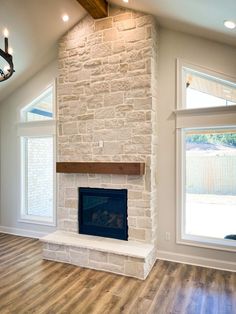 a living room with a fireplace and two windows in the wall, along with hard wood flooring