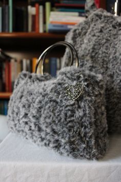 two gray knitted bags sitting on top of a white cloth covered table next to bookshelves