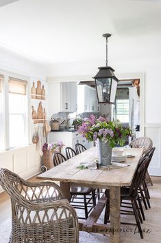 a dining room table with chairs and flowers in a vase on it's centerpiece