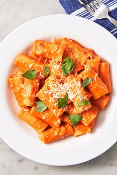 a white plate topped with pasta covered in sauce and parmesan cheese next to a fork