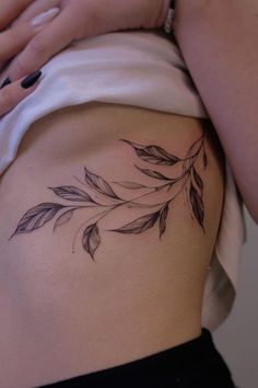 a woman's lower back tattoo with leaves on her side and the bottom part of her stomach