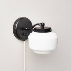 a black and white wall light with a glass shade on it's arm, against a white wall