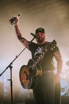 a man with tattoos on his arm holding a guitar and singing into a microphone while standing in front of a microphone stand