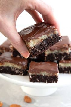 a hand holding a piece of chocolate peanut butter brownie on top of a white plate