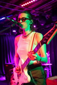 a woman in white shirt playing guitar on stage