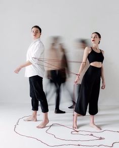 two people standing next to each other in front of a white wall with red string