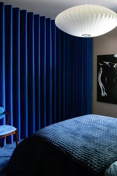 a bedroom with blue curtains and a bed in front of a painting on the wall