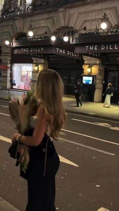 a woman is walking down the street with flowers in her hand and there is an advertisement on the side of the road