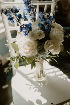 a bouquet of white and blue flowers sitting on top of a table next to a chair