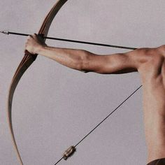 a man with no shirt is aiming an arrow