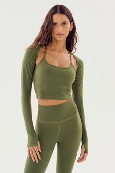 A woman with long hair wears the Shiri Airweight Shrug in Olive, a long-sleeve cut-out crop top by SPLITS59, paired with matching high-waisted leggings made from a nylon-spandex blend. She stands against a plain, light background. Green Sporty Activewear With Thumbholes, Green Comfortable Yoga Activewear, Comfortable Green Yoga Activewear, Green Comfortable Activewear For Yoga, Green Stretch Tops For Pilates, Comfortable Green Activewear For Yoga, Green Athleisure Activewear With Thumbholes, Stretchy Green Tops For Pilates, Comfortable Green Activewear For Gym