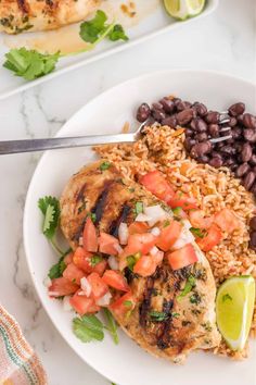 a white plate topped with chicken, rice and black beans next to a lime wedge